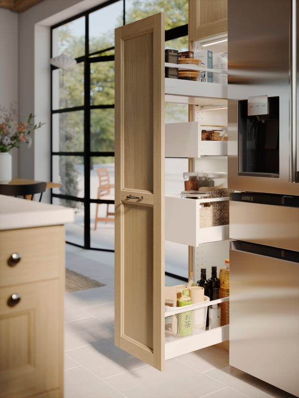 A high cabinet with pull-out drawers and a VEDHAMN door holding food containers and bottles. A patio window is beside it.