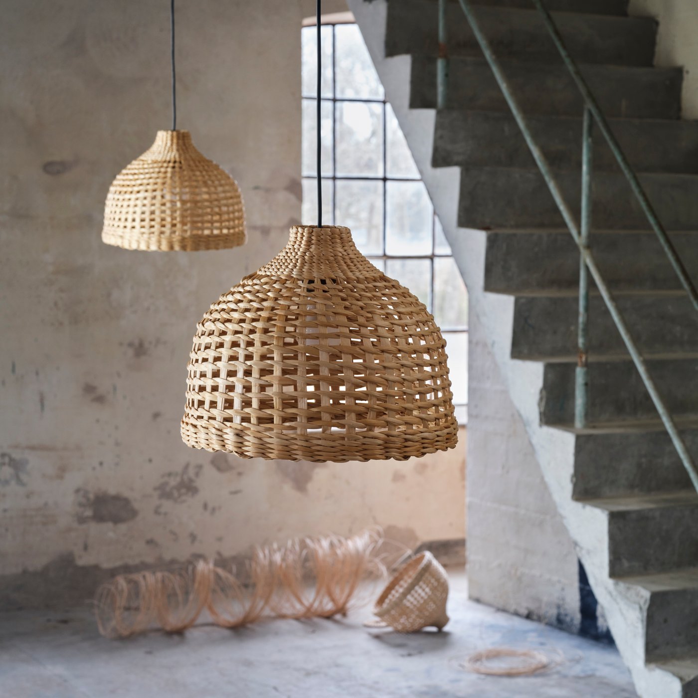 Two MÄVINN lampshades, made from banana fibres, hang from the ceiling next to a staircase in an industrial-looking room.