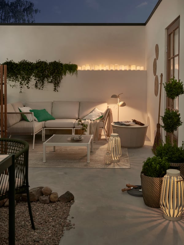 ÄDELLÖVSKOG LED top sveća i SOMMARLÅNKE podne lampe osvetljavaju SEGERÖN baštenski nameštaj na ograđenoj terasi posutoj kamenjem.