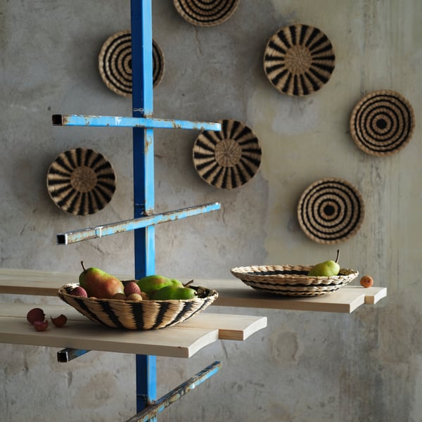 Cinco decoraciones de pared MÄVINN colgadas en una pared gris. Delante, hay dos decoraciones de pared usadas como tazones de fruta.