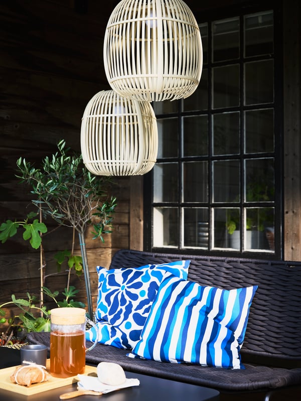 TEGELÖN black sofa with blue and white pillows, a table set with a 365+ carafe of tea, and decorative lighting above.