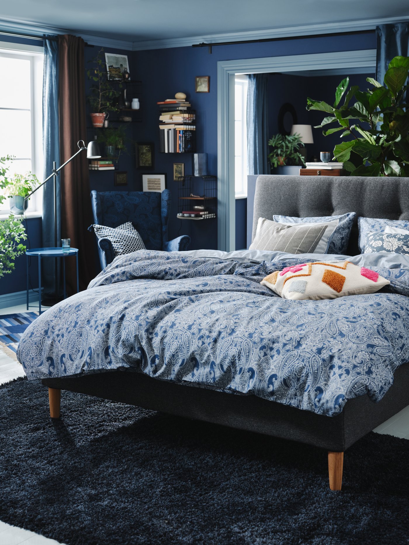 Cama gris IDANÄS con un cobertor JÄTTEVALLMO con diseños en color azul y blanco, en un dormitorio con tonalidades principalmente azules.