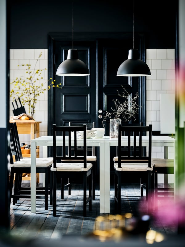 Une salle à manger noir et blanc, deux tables MELLTORP blanches, des chaises STEFAN brun-noir, du carrelage blanc sur les murs et du parquet foncé.