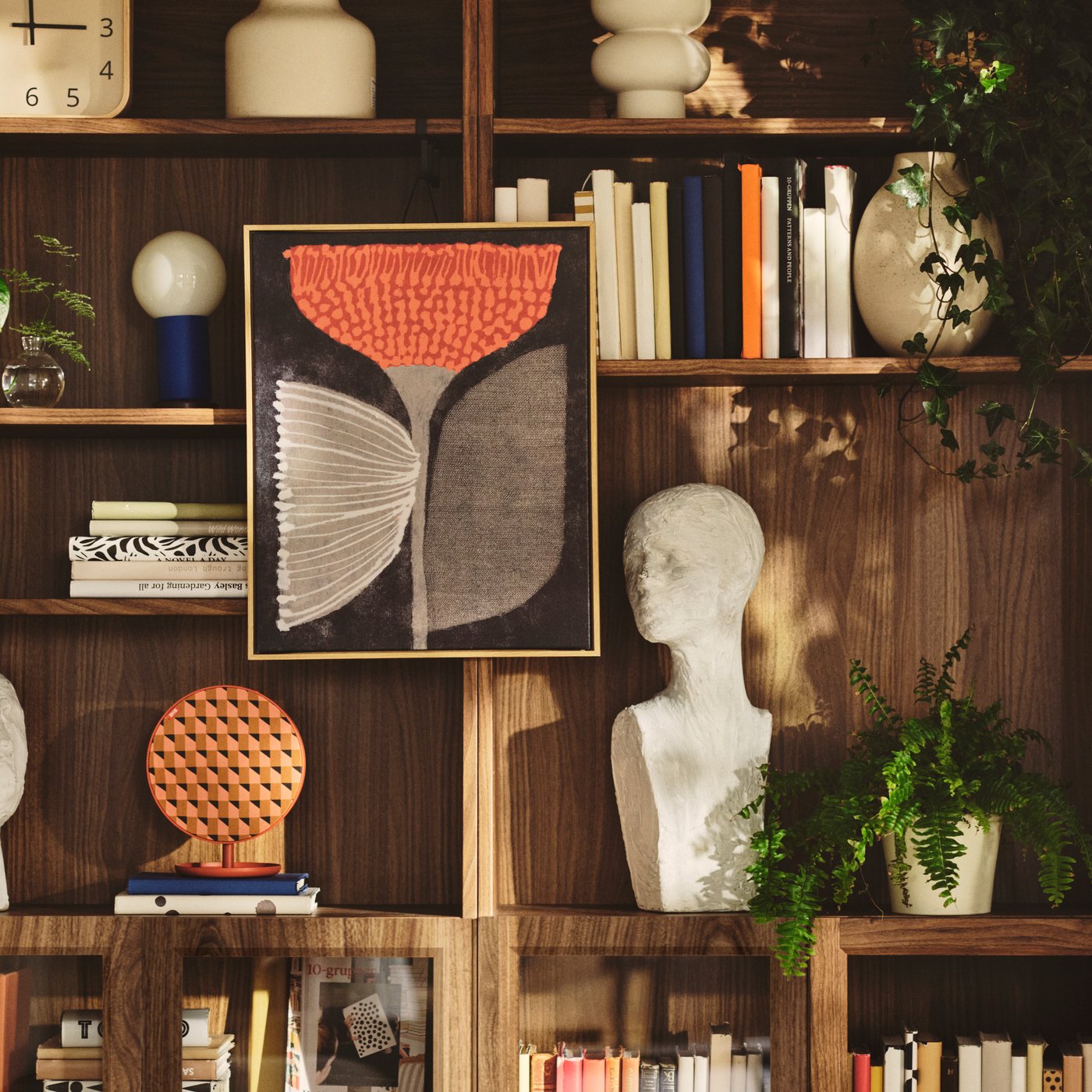 Cuadro BLODFLÄDER con diseño de flor naranja, colocado en una pared sobre repisas de madera con objetos decorativos.