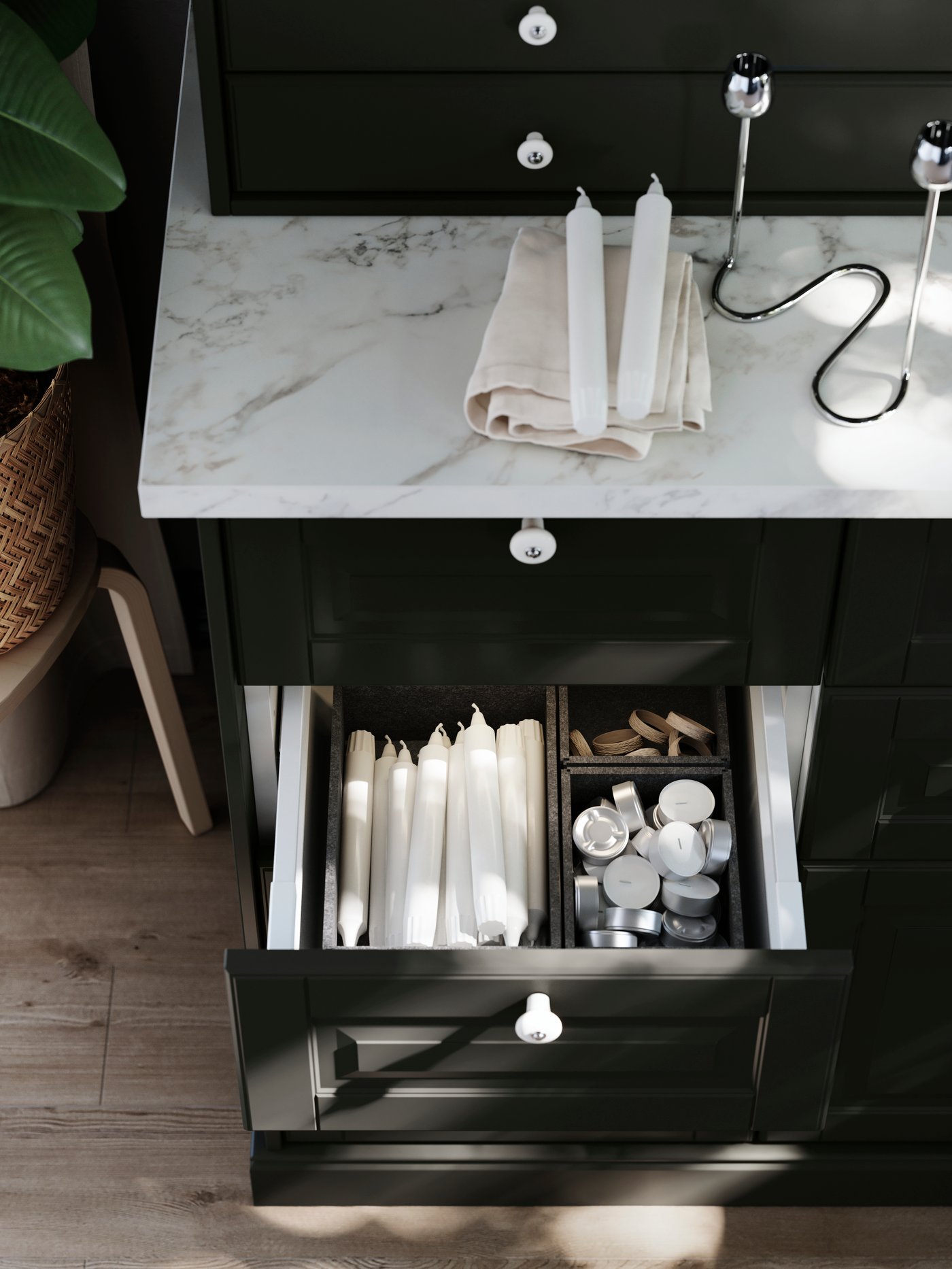 An open drawer in a cabinet with black BODBYN fronts shows interior organisers with dining room items sorted inside them.