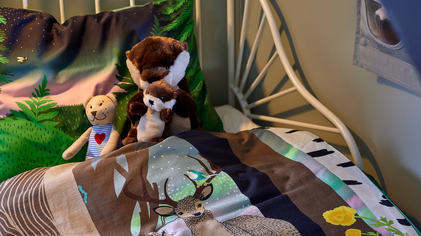 Une partie de lit d’enfant avec linge de lit SKOGSDUVA, des loutres en peluche et l’ourson FABLER BJÖRN.