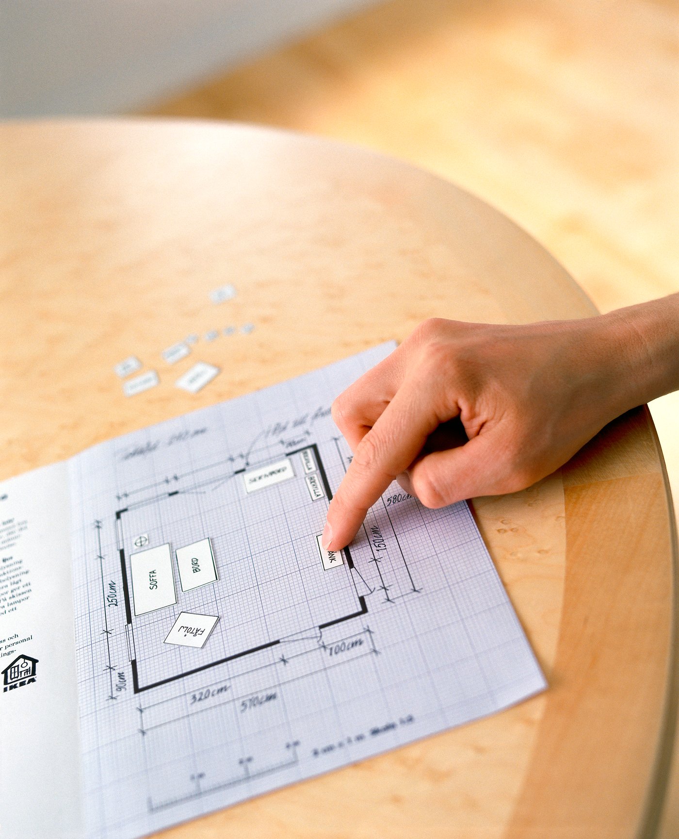 A hand arranging some furniture drawings in a room layout.