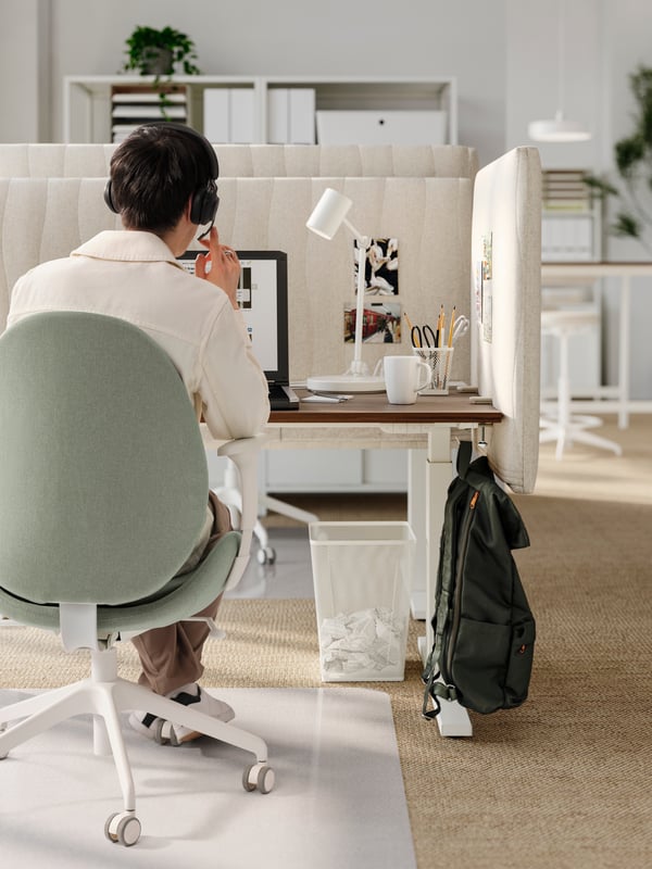 A man with a headset sitting in a green GRÖNFJÄLL office chair at a walnut/white desk with MITTZON acoustic screens for desk.