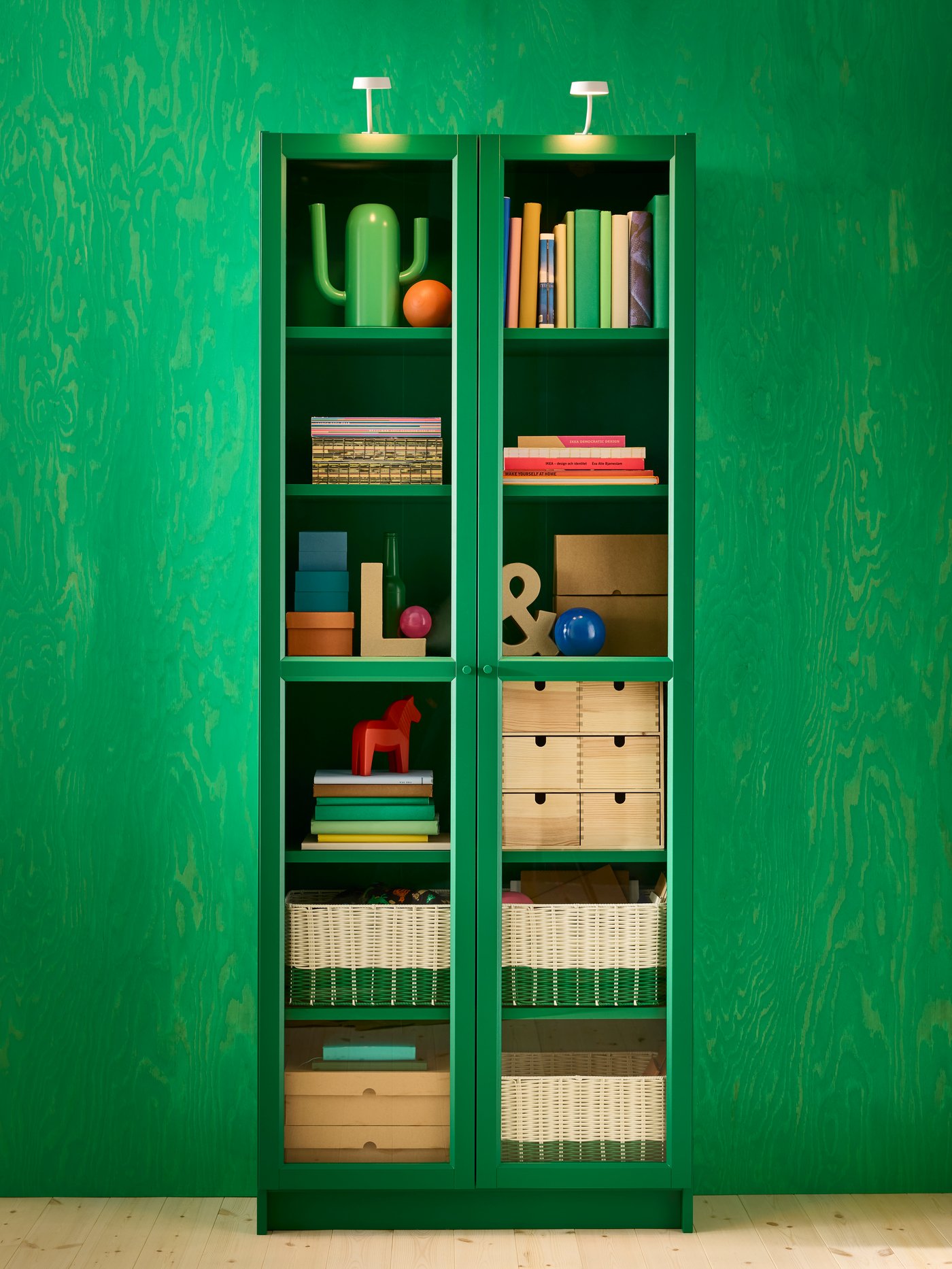 Grande vitrine verte garnie de livres et d’autres objets, devant un mur vert.