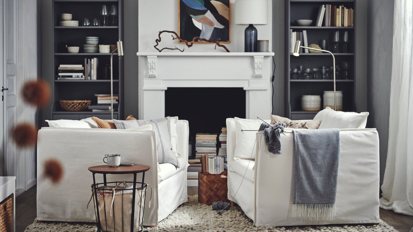 A living room with two facing white BACKSÄLEN armchairs against a backdrop of gray HAUGA high cabinets framing a fireplace.