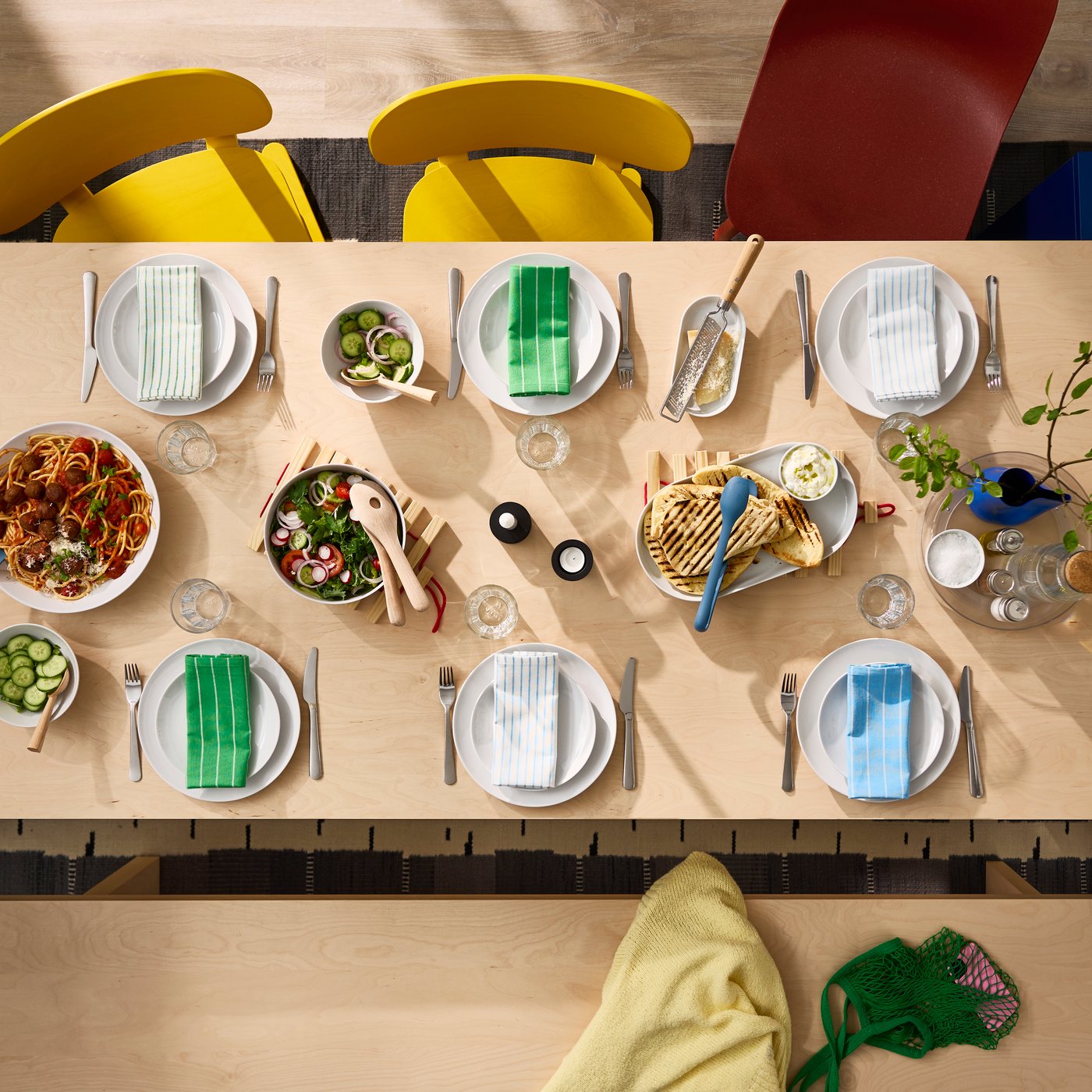 Top view of a set BERGSHYTTAN dining table in birch veneer. Also featured are two yellow chairs and a red ODGER chair.