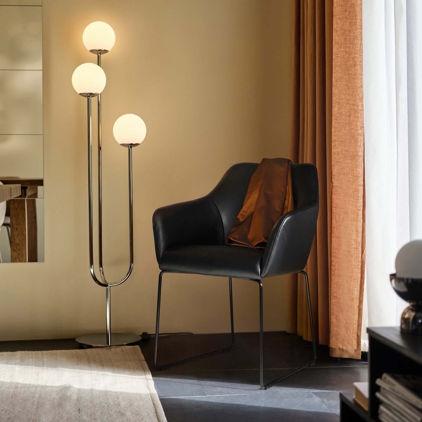 En svart skinnfåtölj står i ett hön av ett rum och bredvid står en modern golvlampa.