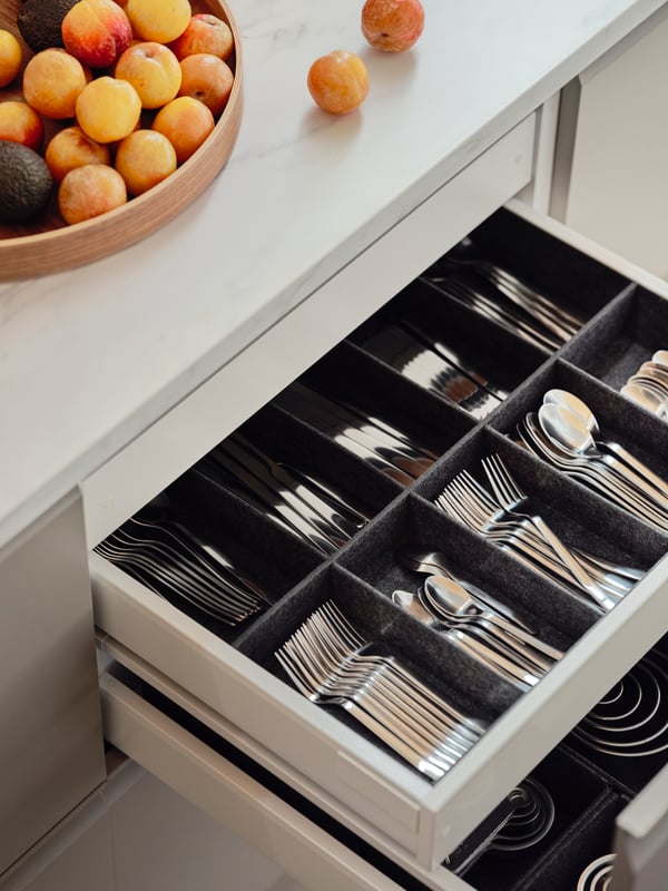A pulled-out kitchen drawer revealing kitchen utensils in plastic and bamboo in UPPDATERA cutlery and utensils trays.
