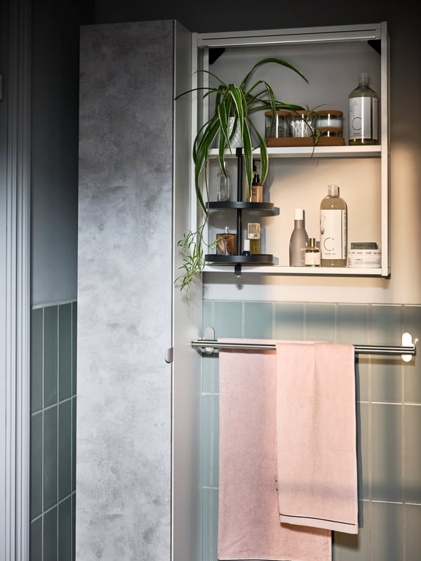 Une salle de bain avec une barre porte-serviettes BROGRUND en acier inoxydable avec une serviette VIKFJÄRD rose et un rangement pour salle de bain ENHET.