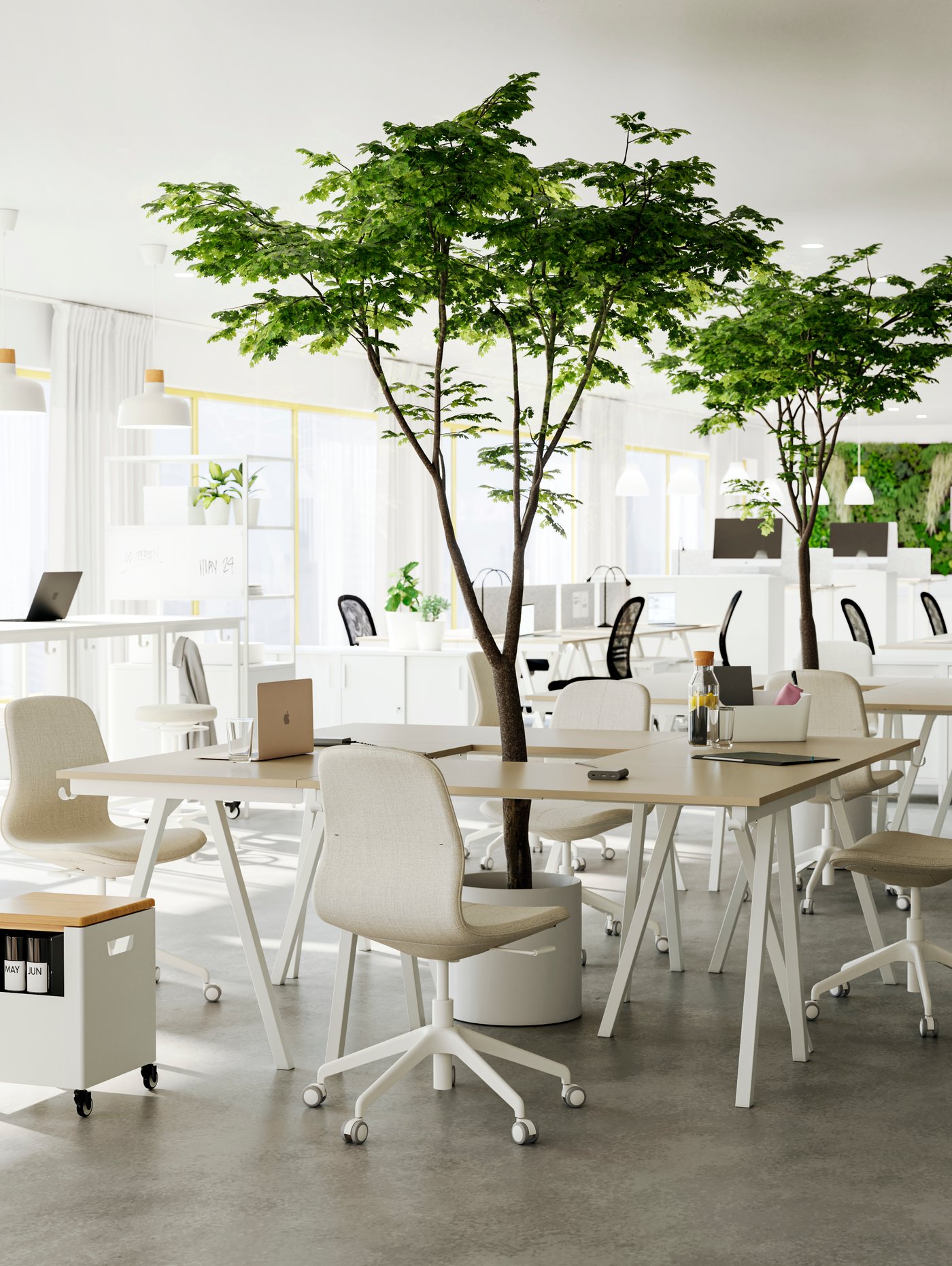 An open office room with several groups of light tables and chairs put together as meeting spots, green plants in between.