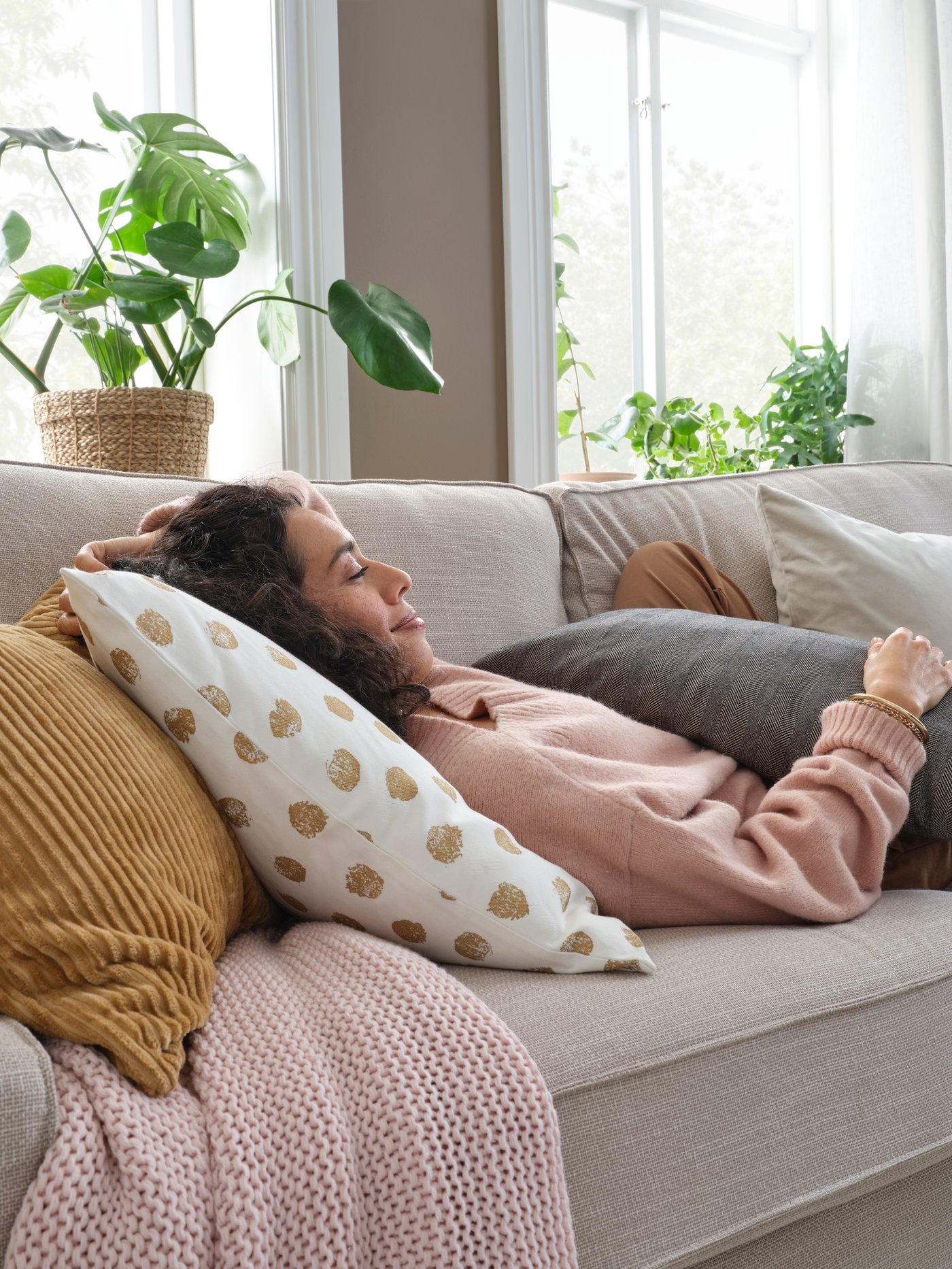 A smiling woman with her eyes closed lies in a grey KIVIK sofa