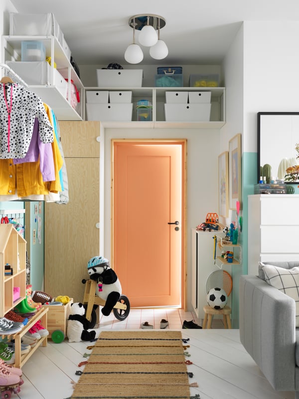 A PLATSA wardrobe, with white PLATSA open shelving units mounted to the wall above it, stands beside a door in a hallway.
