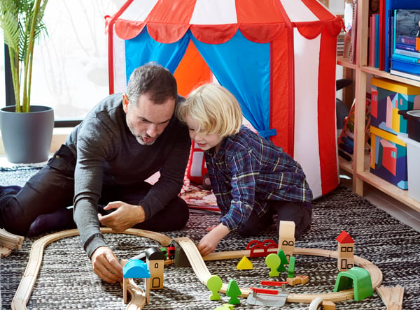En vuxen och ett barn sitter på golvet och leker med ett LILLABO tågset framför ett CIRKUSTÄLT.