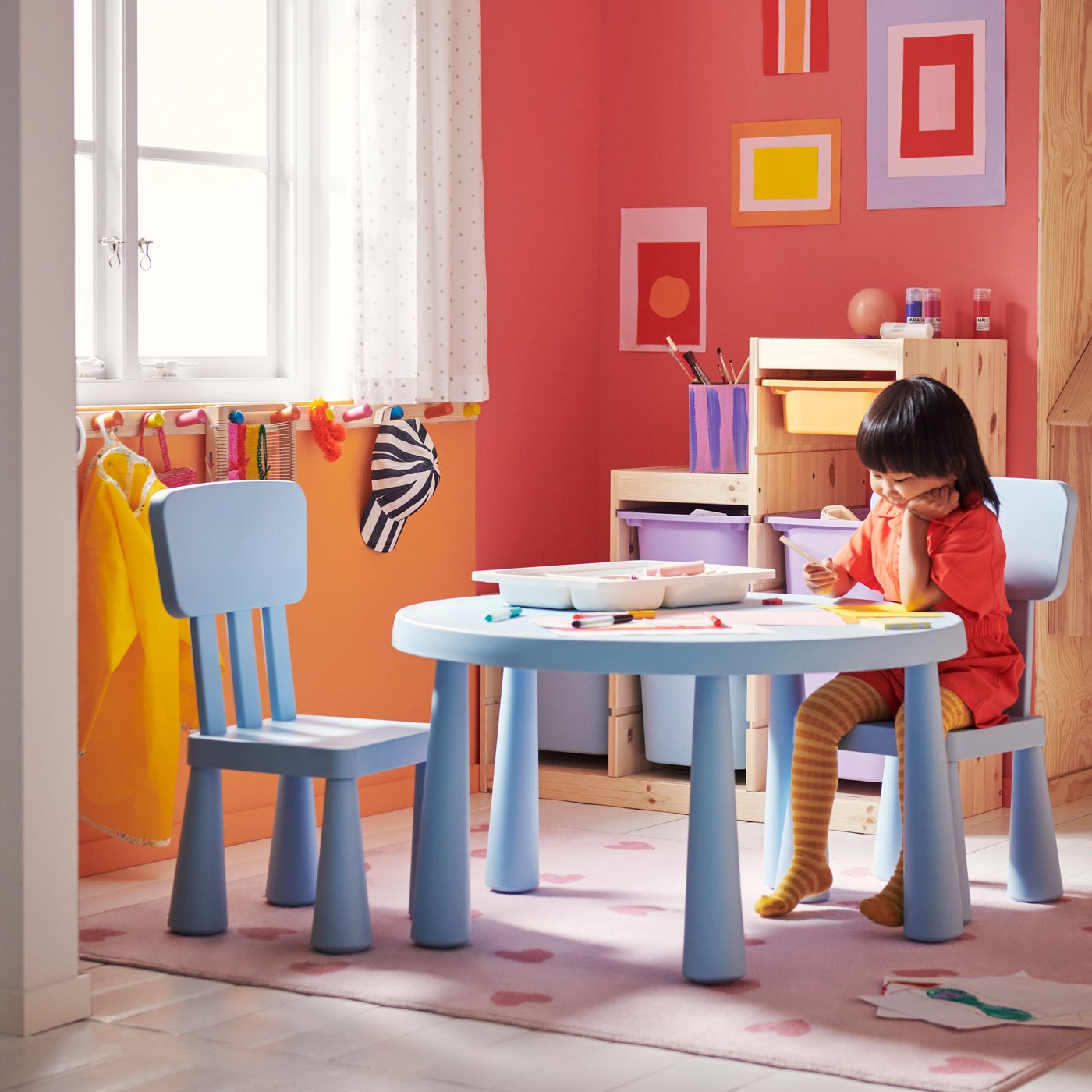 In einem farbenfrohen Kinderzimmer sind zwei Kinderstühle und ein Kindertisch aus der MAMMUT Serie in Hellblau zu sehen.