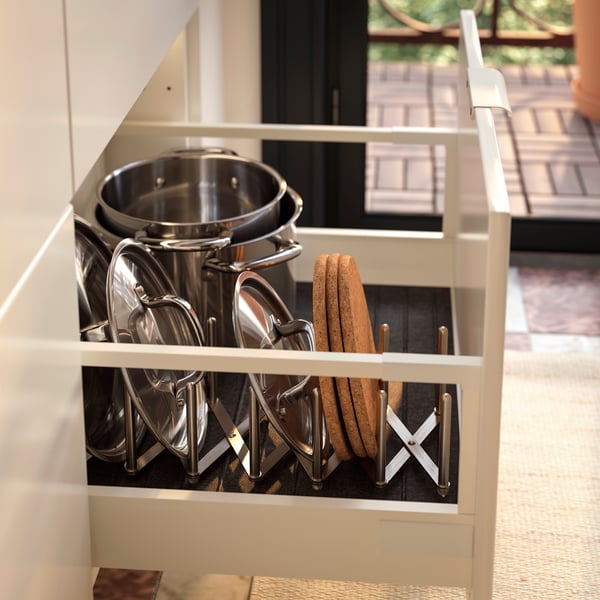 Un mueble de cocina con el cajón abierto y las tapas de las ollas ordenadas gracias a un organizador VARIERA.