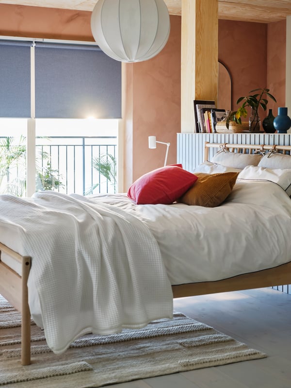 Un letto BJÖRKSNÄS in una stanza con pareti rivestite in legno e la luce che filtra da una finestra IKEA