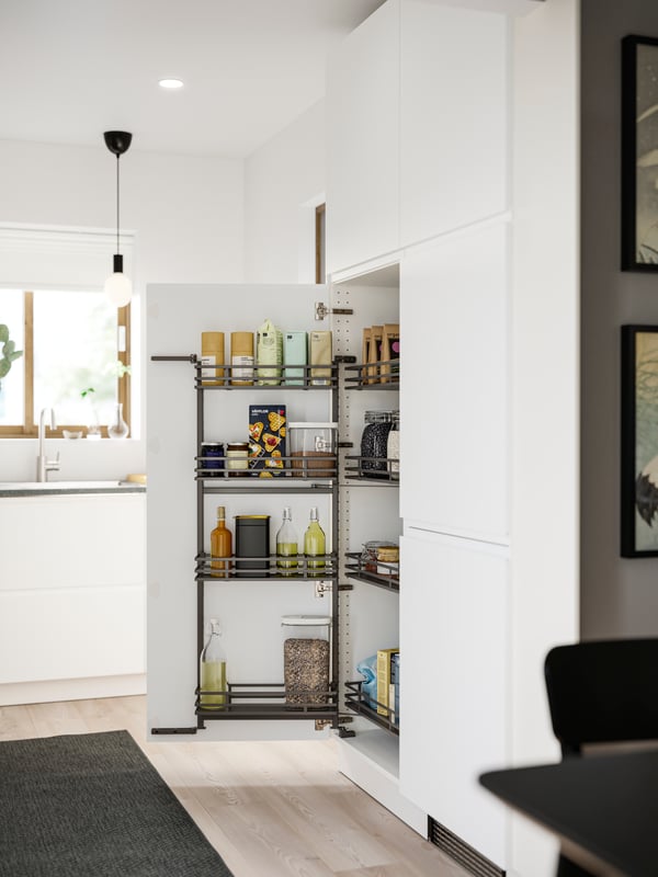 A kitchen with matte white VOXTORP fronts has a UTRUSTA pull-out larder with food packages and containers stored inside.