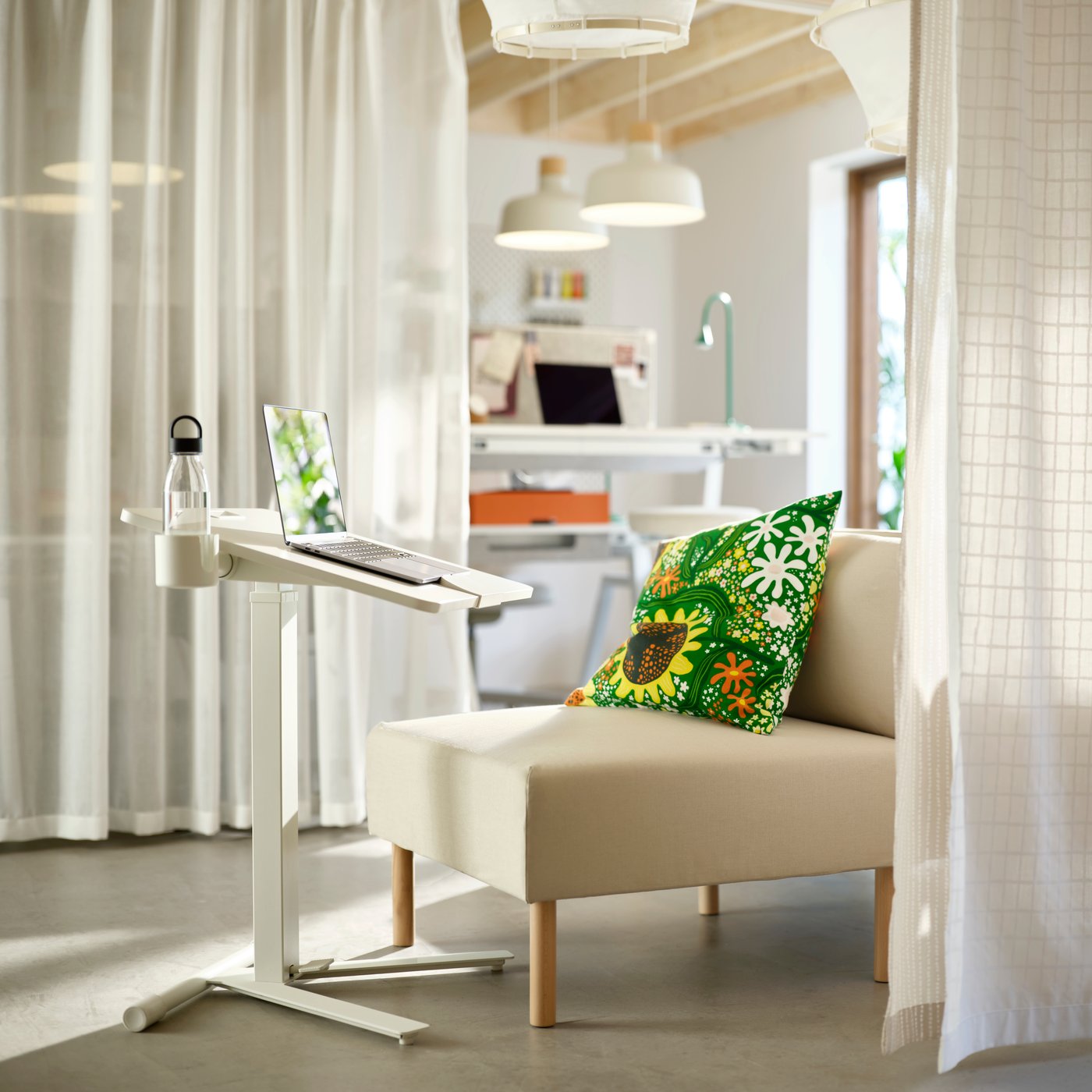 Single white sofa unit with deskstand holding a laptop. Communal workspace in background; divider curtains on either side.