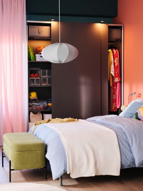 Armoire-penderie PAX/HASVIK gris foncé dont les portes coulissantes sont ouvertes, derrière un lit habillé de linge de lit ÄNGSLILJA gris bleu.