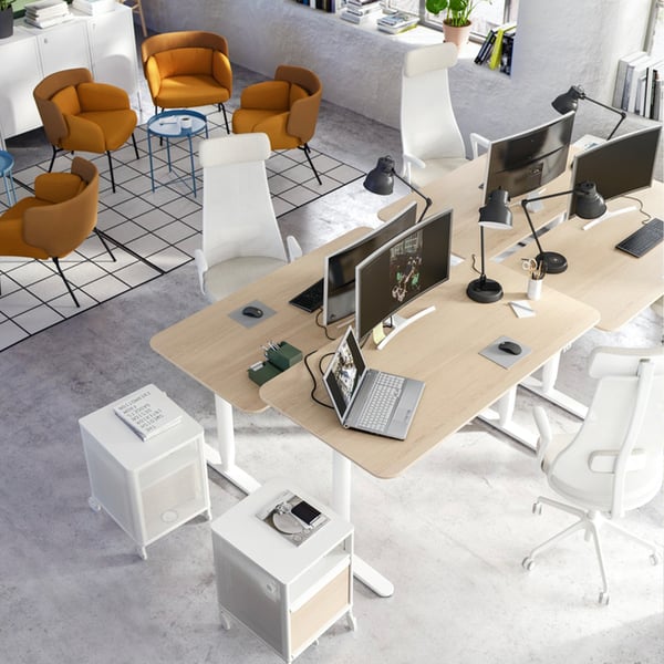 A top view of an office with four chairs and BEKANT desks in oak veneer/white near a lounge area with brown armchairs.