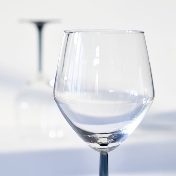 A closeup of the bowl in clear glass of a RÖDRÄKA wine glass with a grey stem, which is standing on a bright surface.