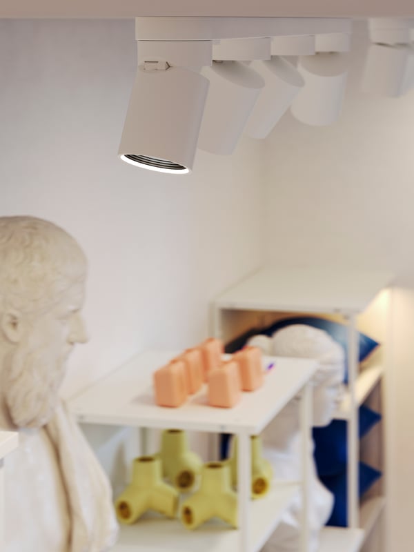Des plafonniers à 4 spots NYMÅNE blancs éclairent des étagères PLATSA fixées au mur dans lesquelles sont exposés des objets déco.