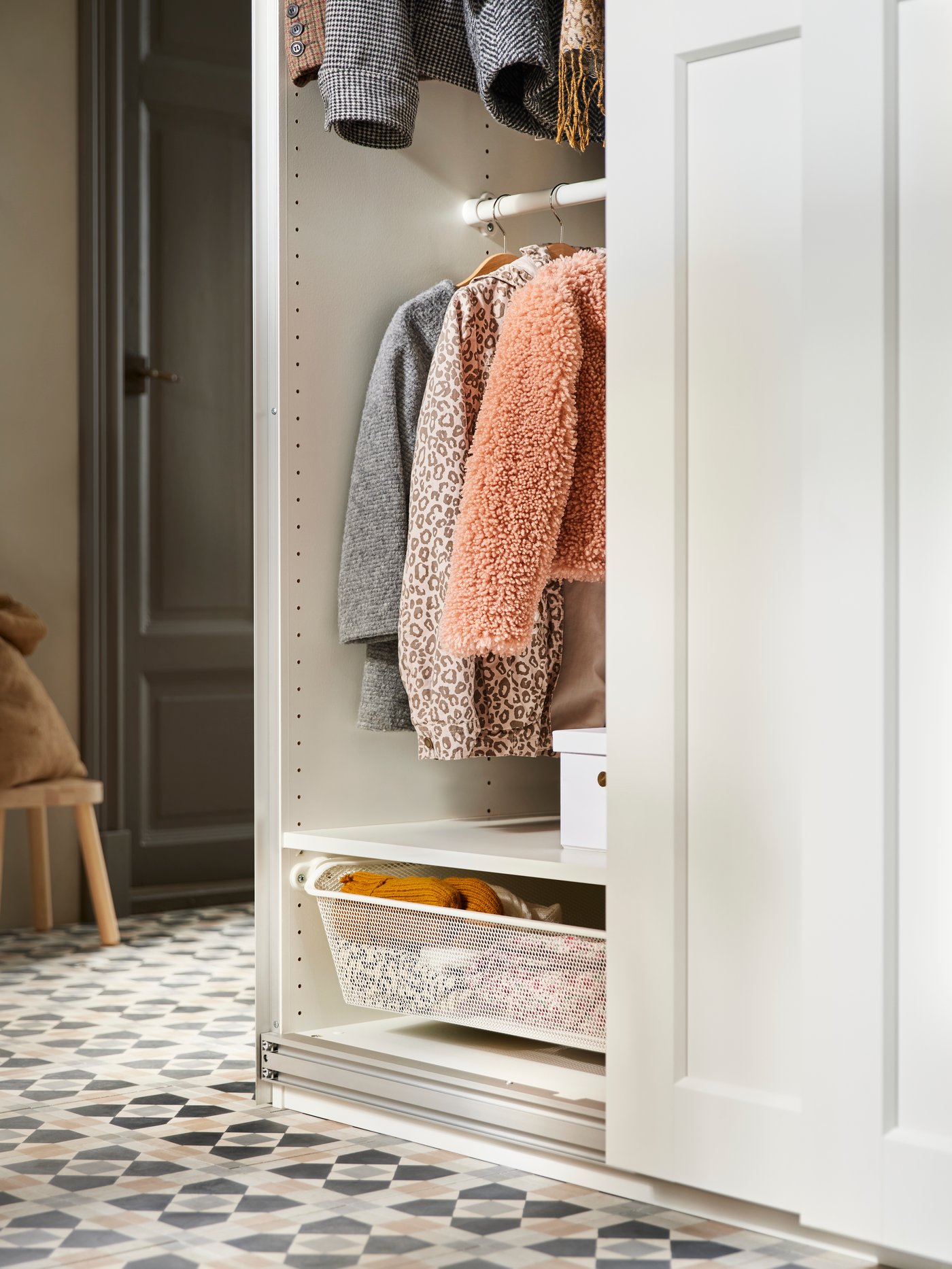An open white PAX wardrobe neatly displays hanging children’s jackets and a pull-out storage basket—a stylish and practical solution for wardrobe organisation.