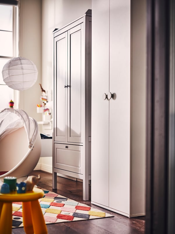 Una recámara infantil con un clóset SUNDVIK gris y un clóset GODISHUS blanco junto a una silla giratoria PS LÖMSK de IKEA.