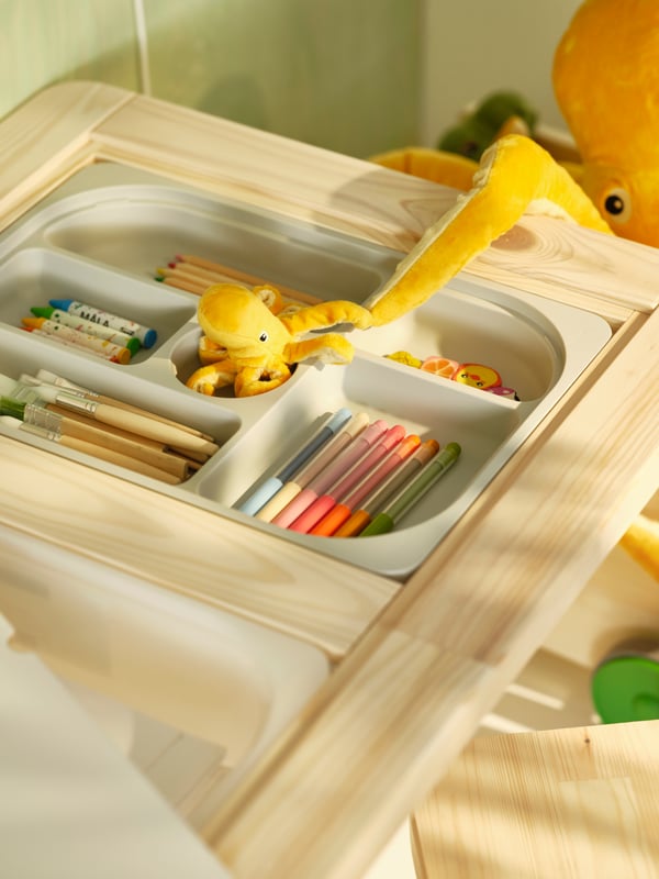 An open drawer of a FLISAT desk shows coloured pencils and crayons organised into different compartments.
