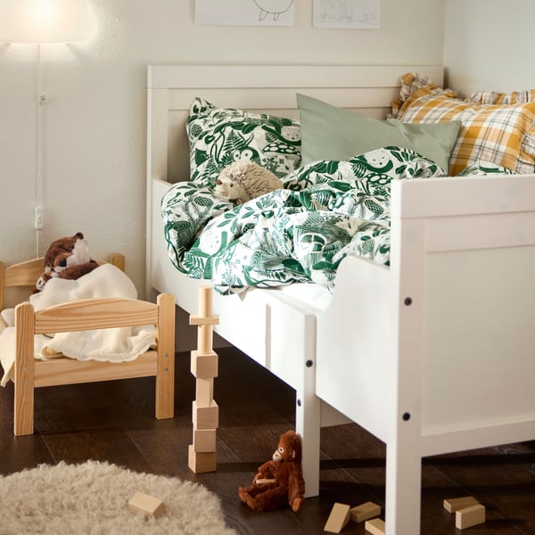 Coin enfant d’une chambre, avec un lit extensible SUNDVIK, un lit de poupée DUKTIG et quelques jouets épars au sol.
