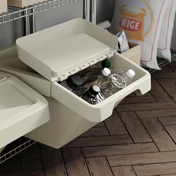 A SORTERA waste sorting bin with lid, partly open and used for recycling plastic bottles in a kitchen pantry.