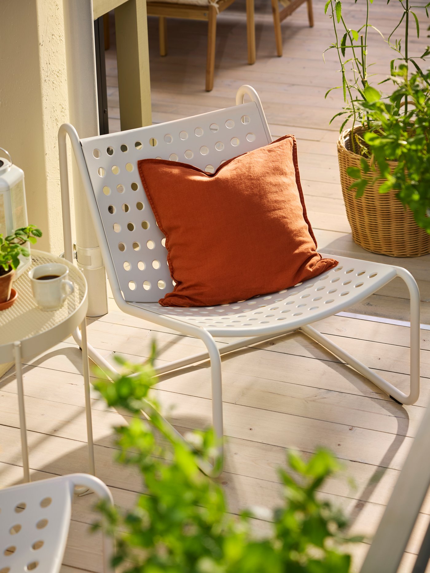 A patio with a light grey SKOGSÖN outdoor easy chair with a reddish-brown cushion, and plants and a side table beside it.