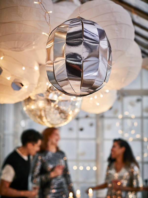 En discokula i silver hänger tillsammans med rislampor i ett växthus.