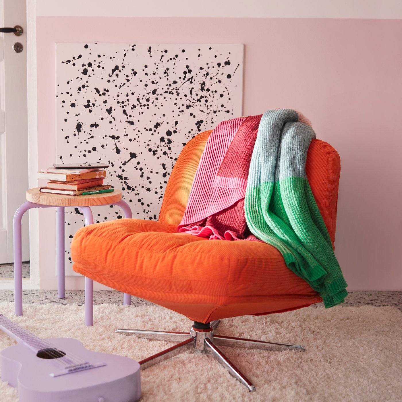 In einem Schlafzimmer liegt eine bunte MARGOSATRÄD-Decke auf einem orangefarbenen DYVLINGE-Drehsessel von Kelinge.