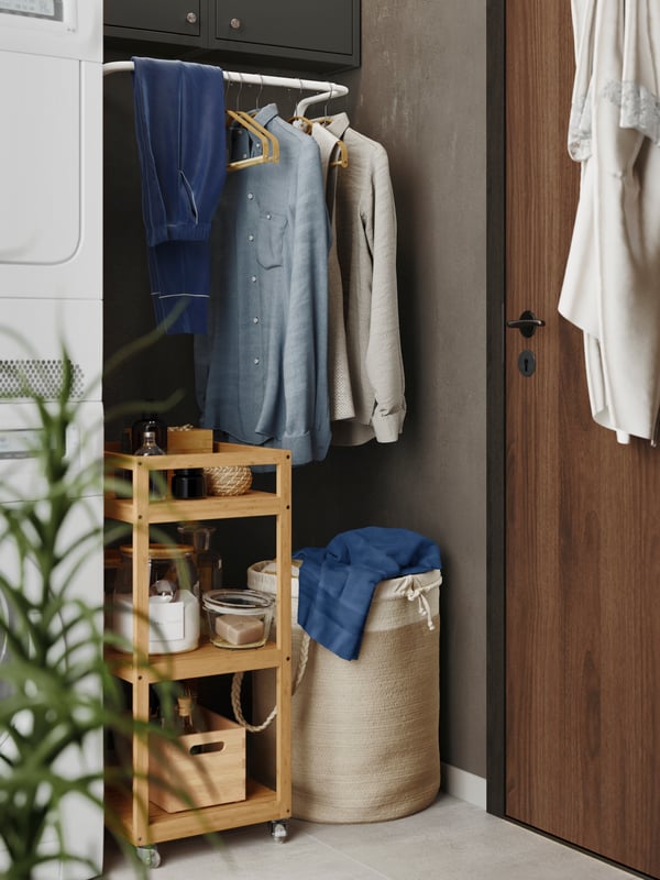 Un coin de la salle de lavage contenant un portant avec des vêtements suspendus, une desserte en bois et un panier à lessive. 