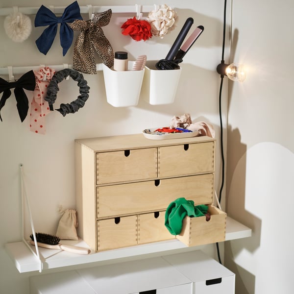 A pine MOPPE mini chest of drawers on top of a white BERGSHULT shelf holds hair accessories, with two hook rails above it.