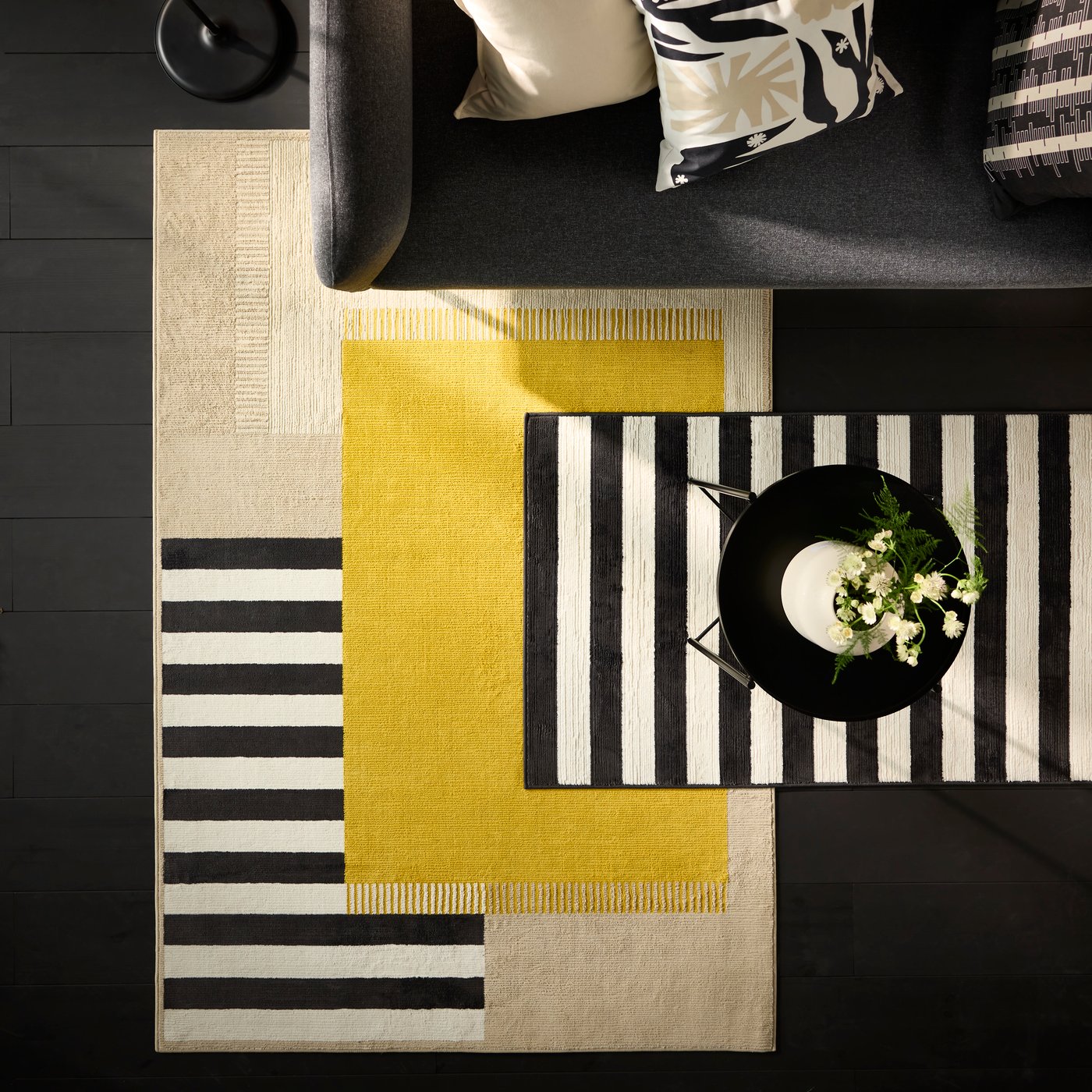 A multicolour ELSYSTEM low pile rug placed by a sofa is partly covered by a black and white rug with a tray table on it.