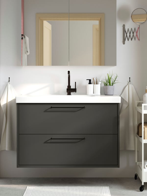 Vista frontale di un mobile per lavabo HAVBÄCK con cassetti, grigio scuro, e di un lavabo ORRSJÖN con sopra un mobile a specchio.