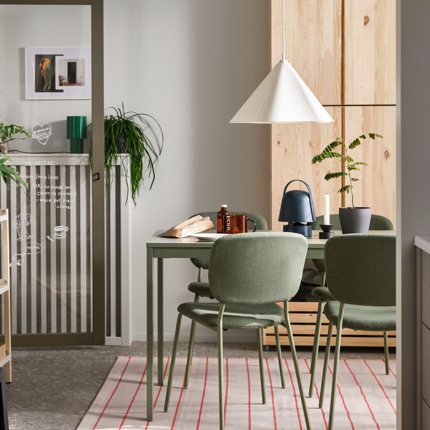 In einem Esszimmer stehen VIHALS Stühle an einem grünen VIHALS Ausziehtisch, der auf einem Teppich steht. Über dem Tisch hängt eine ZEBRASÄV Hängeleuchte.