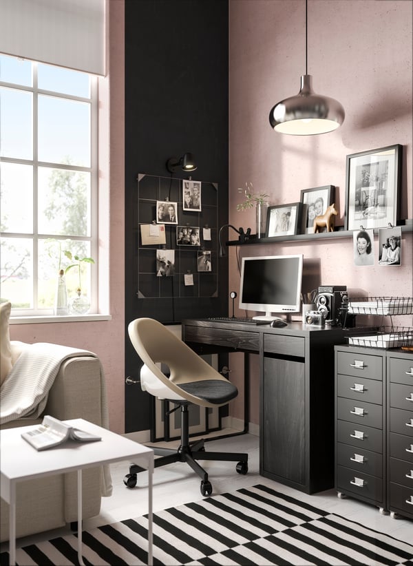 Al costado de un sofá en una sala hay un escritorio MICKE IKEA negro con cajones.