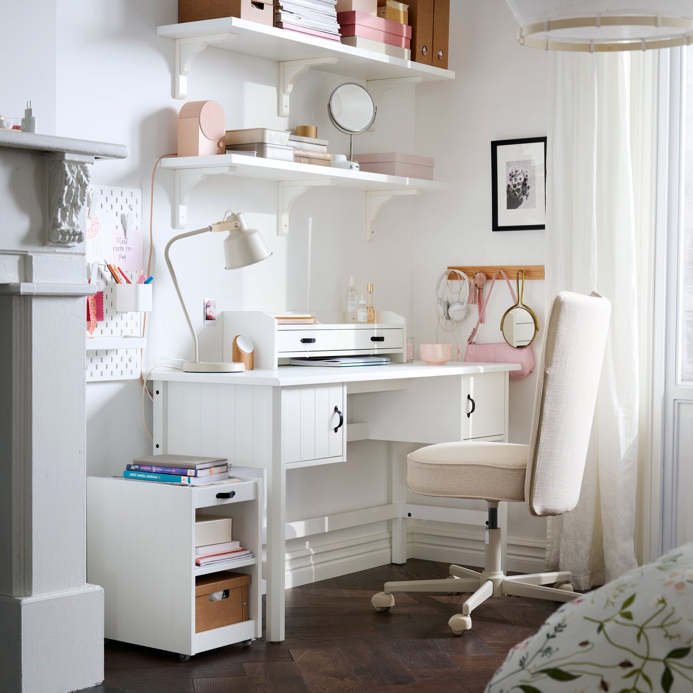 A bedroom with a white BRYTNING desk made from white material sits beside a bed with floral bedding.