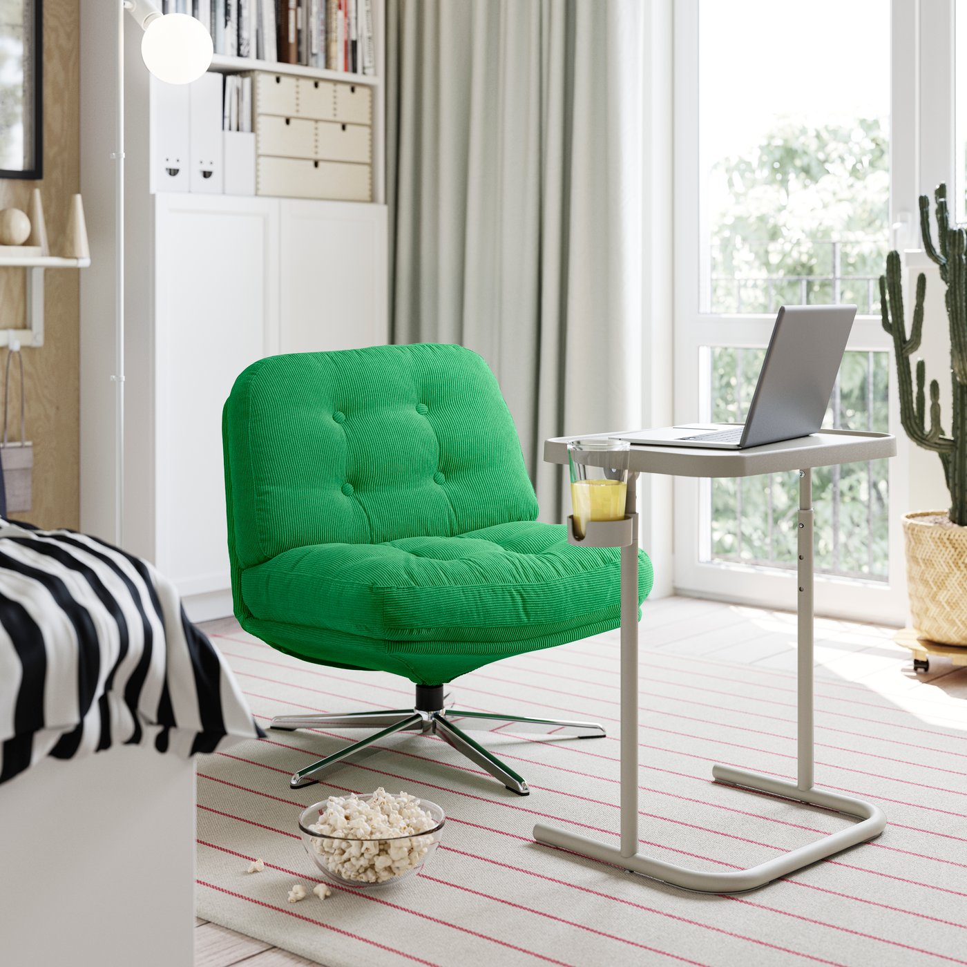 An armchair with a BJÖRKÅSEN laptop stand in grey in front of it, with a cup of juice in the holder.