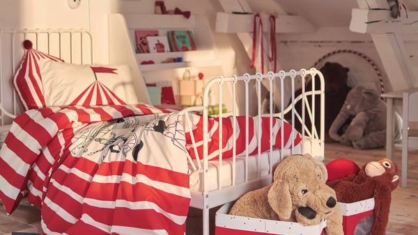 Un lit extensible MINNEN turquoise dans l’angle d’une chambre pour enfants, avec des jouets, une lampe de bureau et des rangements.