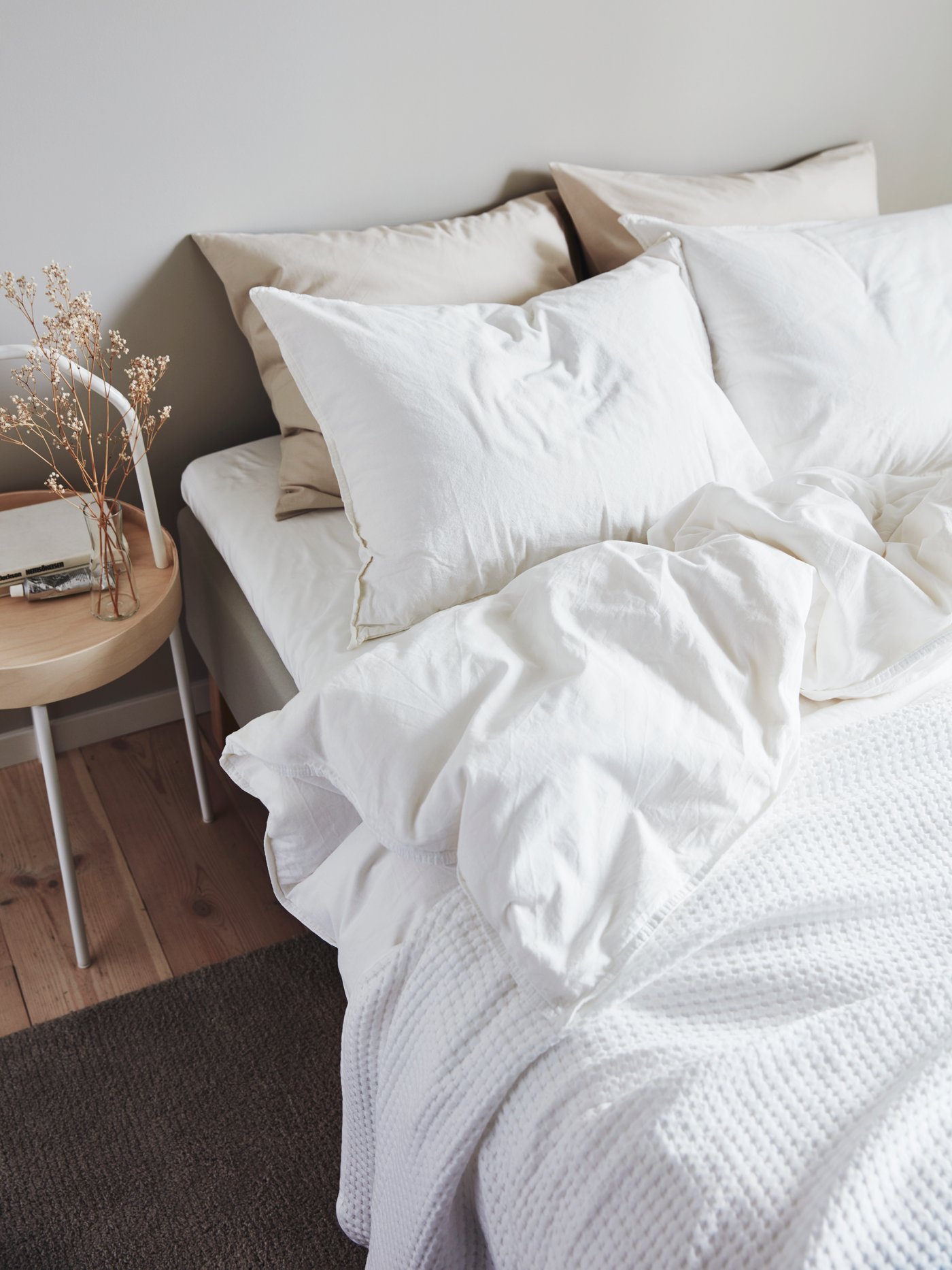 VÅRELD bedspread blanket in white on a white bed. A stool acts as a nightstand with books resting on top of it