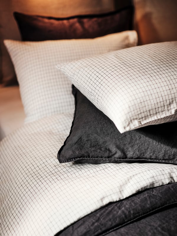 A bed dressed in a white black/check ÅKERFIBBLA duvet cover with 2 pillowcases and a DYTÅG duvet cover with 2 pillowcases.